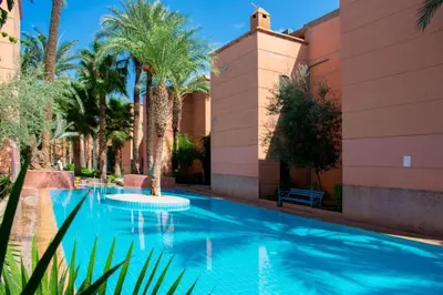 a swimming pool with palm trees in front of a building at Al Qaria Syahia Duplex Moufid in Marrakech