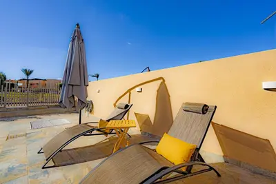 a patio with two chairs and an umbrella at M REVASION Appt 3 chambres , front de lac , piscine chauffée privée in Marrakech
