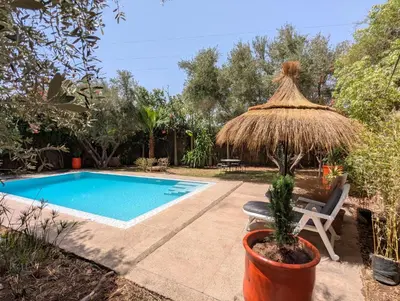 a pool with a straw umbrella and a chair next to it at Oasis Villa in Marrakech