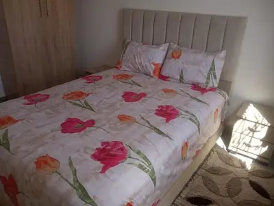 a bed with a floral bedspread with red roses on it at Menara Airport Appartement - 10 Min Walk in Marrakech
