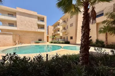 a swimming pool in front of a building with a palm tree at Apartment in Agdal with Pool and Terrace in Marrakech