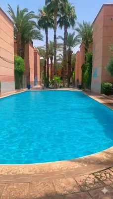 a large blue swimming pool with palm trees and buildings at Riad Nahara in Marrakech