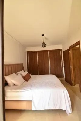 a bedroom with a white bed with a wooden headboard at Superbe T2 neuf - Proche centre - Piscines et Balcon - Marrakech in Marrakech