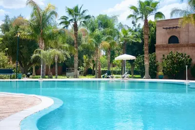 a swimming pool with palm trees and a building at Marrakxi in Marrakech