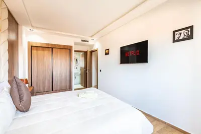 a bedroom with a large white bed with a tv on the wall at Appart 3 CH Menara Garden in Marrakech