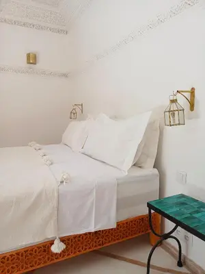 a white bed with white pillows and a green table at Riad DabaKech in Marrakech