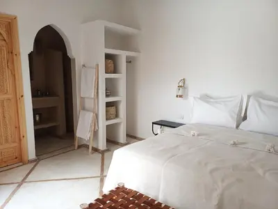 a white bedroom with a bed and a book shelf at Riad DabaKech in Marrakech