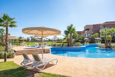 two chairs and an umbrella next to a swimming pool at Luxury Apartment - Prestigia Golf City Marrakech in Marrakech