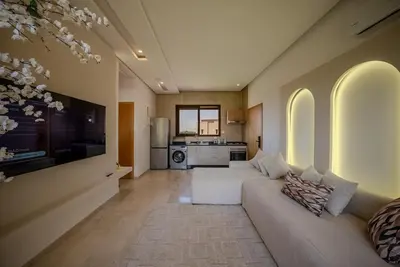 a living room with two white couches and a kitchen at Prestigia Apartment Secure Residence Pool in Marrakech