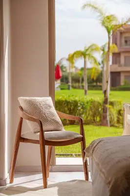 a chair sitting in front of a window in a bedroom at Le Lys - Prestigia Argan - Golf - 6 Prs - Piscine in Marrakech