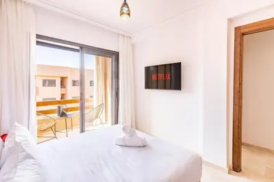 a white bedroom with a bed and a balcony at Pool views 2BR family apartment in Marrakech