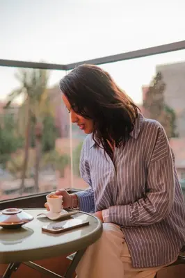 a woman sitting at a table with a cup of coffee at Chill Repeat Designer 2BR 2BA In Central Gueliz in Marrakech