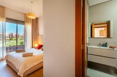 a bedroom with a bed and a bathroom with a window at Appartement de charme vue piscine et espace vert in Marrakech