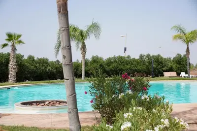 a swimming pool with a palm tree and flowers at Appartement XXL résidence privée piscine Dar Dmana PALMERAIE in Marrakech