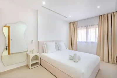 a white bedroom with a white bed and a mirror at Appartement chic près de la gare in Marrakech