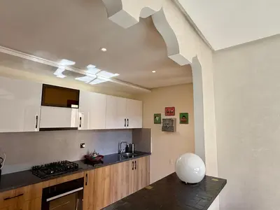 a kitchen with white cabinets and a black counter top at TERRASSE, 2 CHAMBRES SPACIEUSES, 6 COUCHAGES, 2 PiSCINES, PARKING, IDÈAL FAMILLE in Marrakech