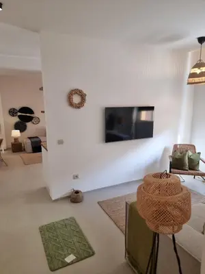 a living room with a white wall with a tv at Bohemian & Moroccan Apartment Close to Airport & Medina in Marrakech