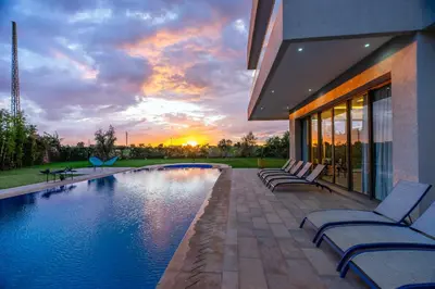 a house with a swimming pool with chairs and a sunset at Golfside Villas in Marrakech