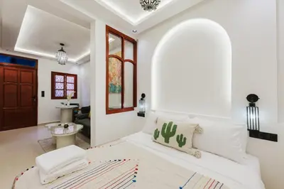 a white bedroom with a bed and a living room at Maison Joudia in Marrakech