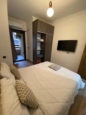 a bedroom with a large white bed with a flat screen tv at Appartement 1 chambre à Gueliz Confort et piscine in Marrakech