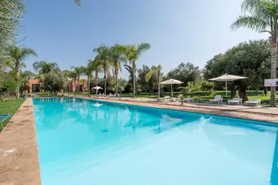 a large blue swimming pool with palm trees and umbrellas at Appartement rooftop privatif Vizir Center in Marrakech