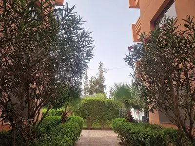 a walkway between two buildings with trees and bushes at Appartement 2 chambres, piscine, vue palmeraie in Marrakech