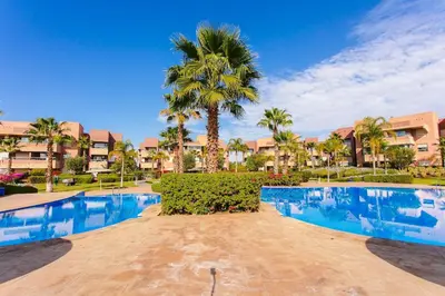 a resort swimming pool with a palm tree and buildings at Your Tiny Paradise - Marrakech - Prestigia in Marrakech