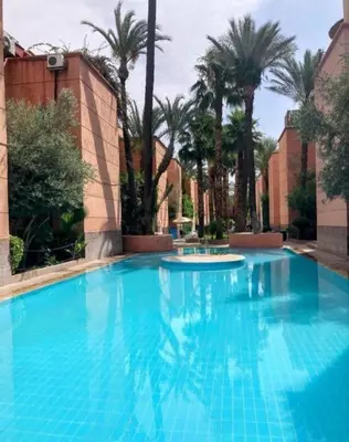 a large blue swimming pool with palm trees in the background at Riad Zellige 95 in Marrakech