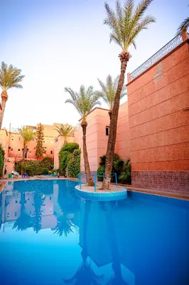 a swimming pool with palm trees in front of a building at Riad 3ch, proche Médina, résidence avec piscines in Marrakech