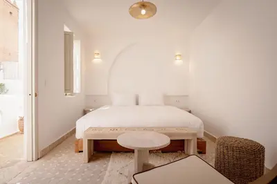 a white bedroom with a bed and a stool at Riad KECH LeS ESSENTIELS in Marrakech
