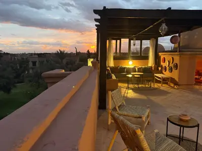 a rooftop patio with chairs and a sunset in the background at Atlas golf resort beldi chic piscine in Marrakech