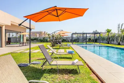 an orange umbrella and chairs next to a swimming pool at Spacious villa with jacuzzi and activities in Marrakech