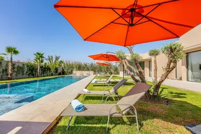 a pool with two chairs and an orange umbrella at Spacious villa with jacuzzi and activities in Marrakech