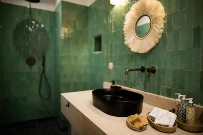 a green tiled bathroom with a sink and a mirror at Riad A l'Ombre du Palais in Marrakech
