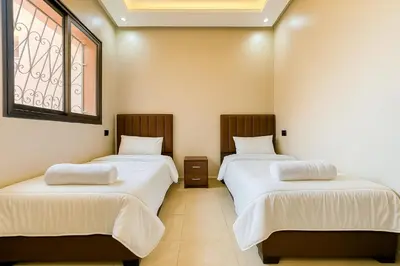 a room with two beds with white sheets and a window at Appartement Confort & Sérénité Mabroka Marrakech in Marrakech