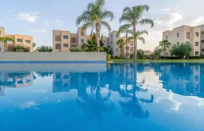 a pool of blue water with palm trees and buildings at Appartement luxe avec vue imprenable sur le golf in Marrakech