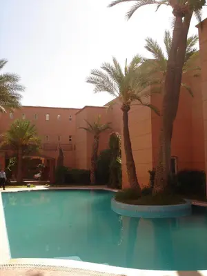a swimming pool with palm trees in front of a building at Riad Nora - Confort, Calme & Sécurité in Marrakech