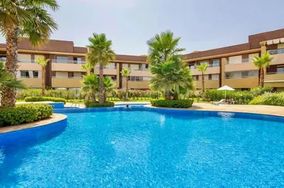 a swimming pool in front of a building with palm trees at Prestigia Agate 5 minute from Airport in Marrakech