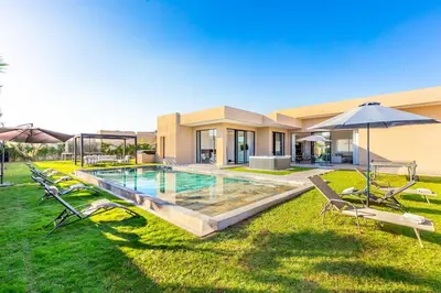 a house with a swimming pool with chairs and an umbrella at Prestige Twin Villa with Splendid View in Marrakech