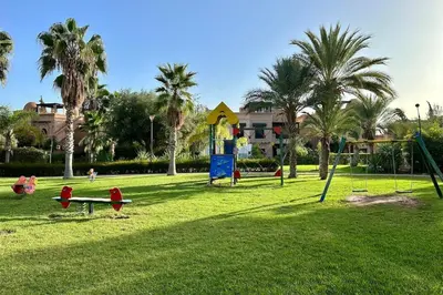a park with a playground with palm trees and a building at Atlas Golf Resort with Terrace and Pools in Marrakech