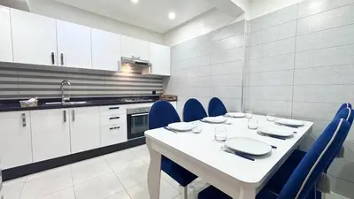 a white kitchen with a white table and blue chairs at Duplex Élégance et Confort avec piscine au Cœur de Marrakech in Marrakech