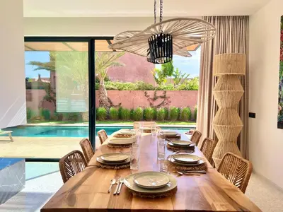 a dining room table with chairs and a large window at Villa AYA - Moderne & Chic in Sraghna
