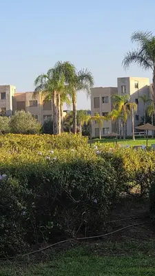 a building with palm trees and a field of bushes at Spacious Ground Floor Oasis with Pool & Golf Course View 1rom in Marrakech