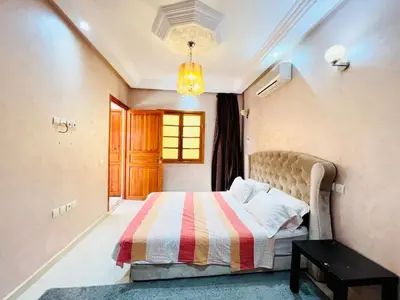 a bedroom with a bed and a table and a window at Cycas Family aparts 1 ch salon parking in Marrakech