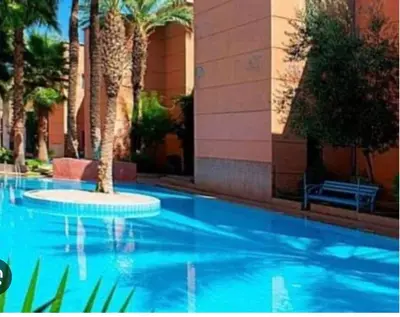 a blue swimming pool with palm trees and a building at Appartement au centre de Marrakech in Marrakech
