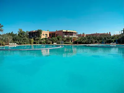 a large pool of blue water with buildings in the background at Oasis Palmeraie - Piscines & terrasses in Marrakech