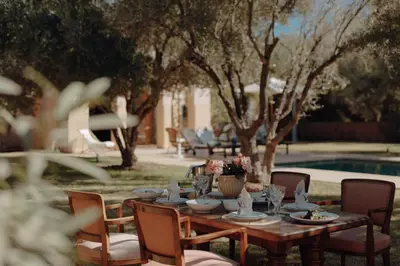 a wooden table and chairs with a table and a pool at Casa Memoria Marrakech in Marrakech