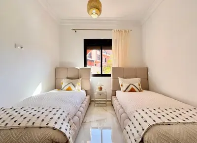 two beds in a room with white walls and a window at Appart cosy & chic premium Village, 5 piscines in Marrakech