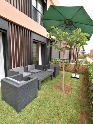 a patio with couches and a green umbrella and a tree at Marrakech Noria Golf, cosy appartement 2 chambres in Marrakech