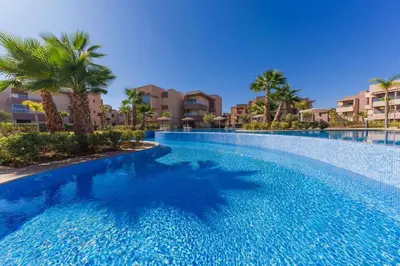 a large swimming pool with palm trees and buildings at Spacious 2BR , Pool & Garden , Golf View , Fast WiFi in Marrakech